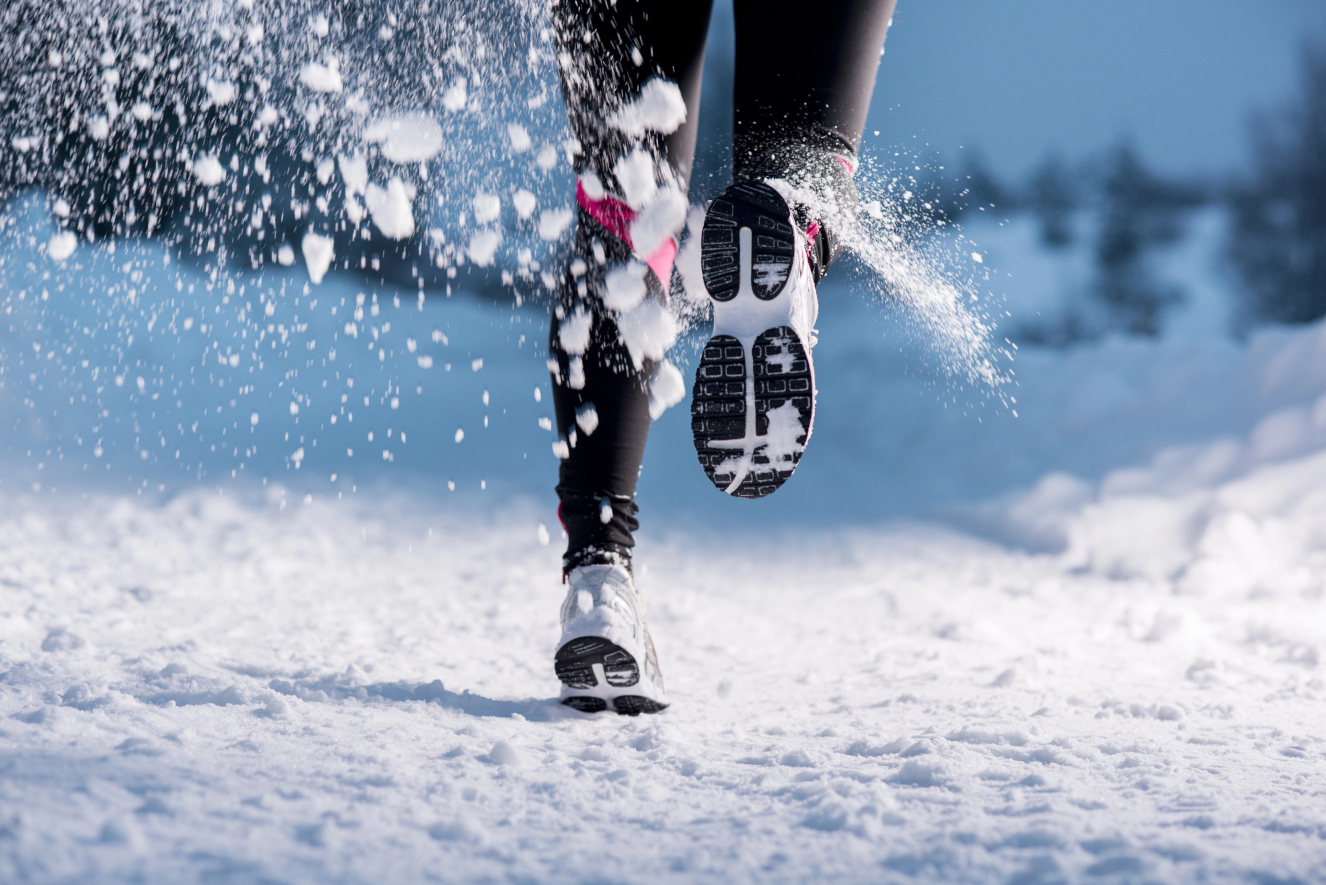 Outdoor-Training im Winter: Läuferin joggt durch verschneite Landschaft und wirbelt Schnee auf
