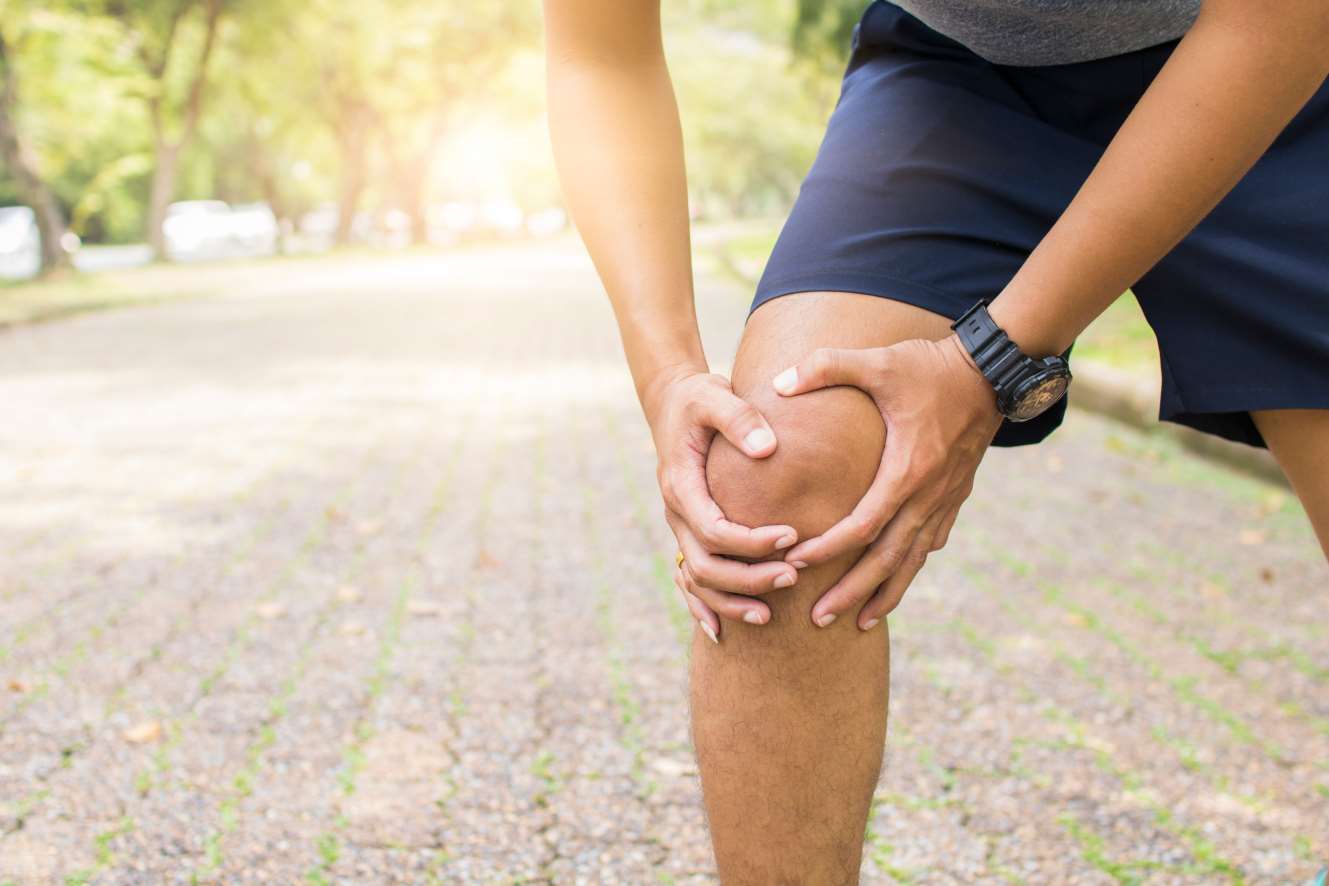 Ein Mann hält sein schmerzendes Knie beim Sport im Freien.