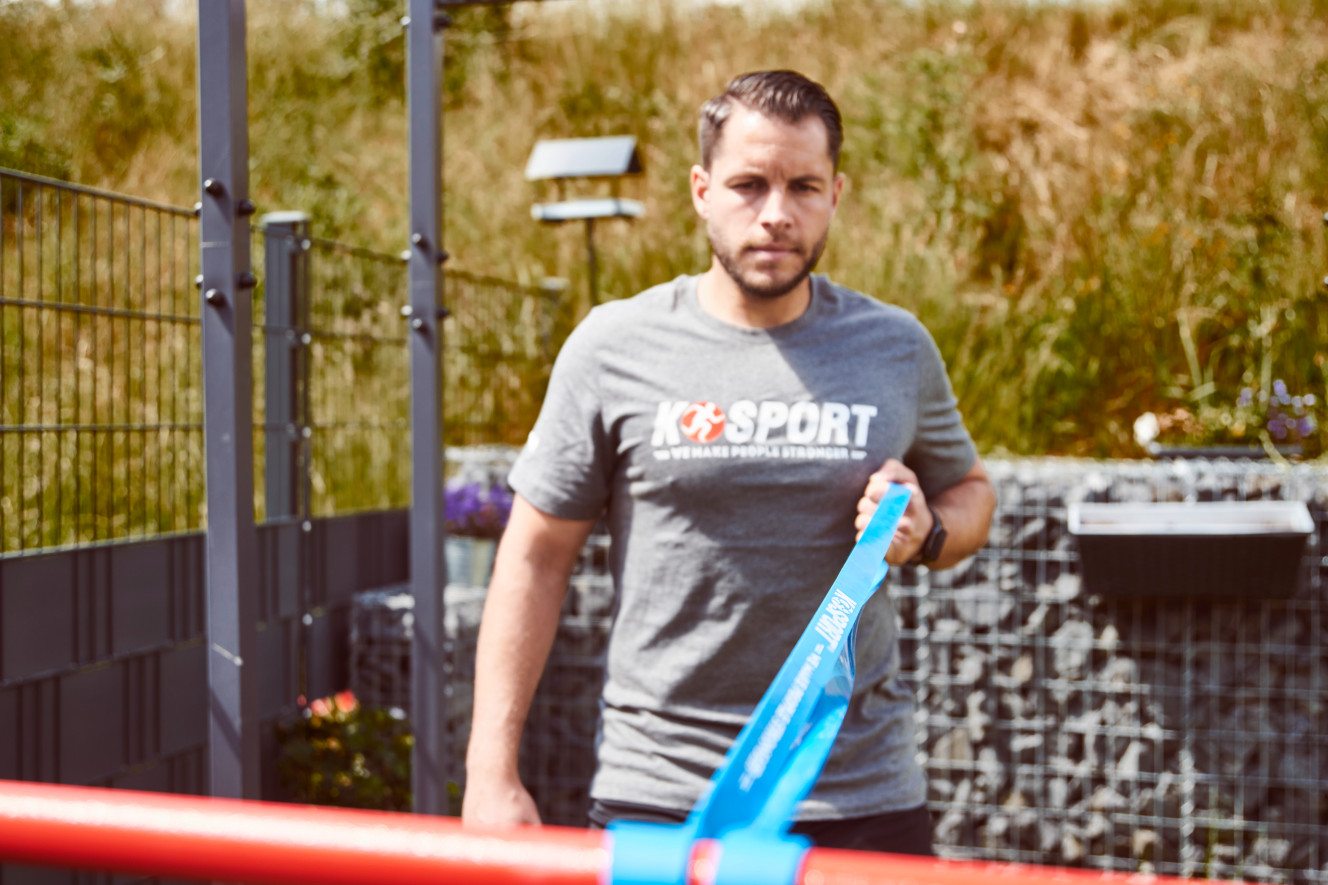 Mann führt Warm-up Übung mit K-Sport Widerstandsband im Homegym aus, ideal zum Aufwärmen und Cool-down Workout