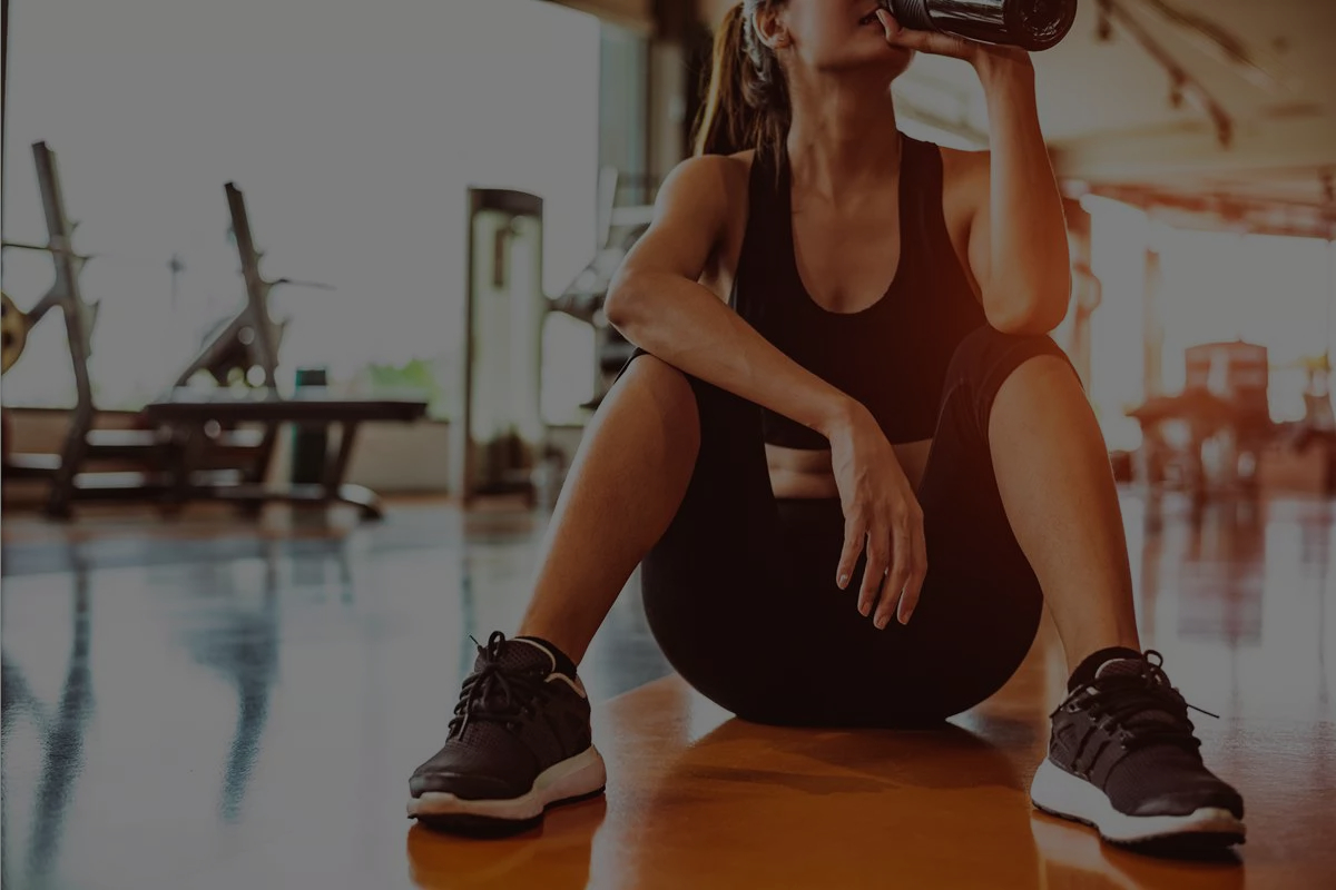 Frau sitzend mit Trinkflasche in Fitness-Studio