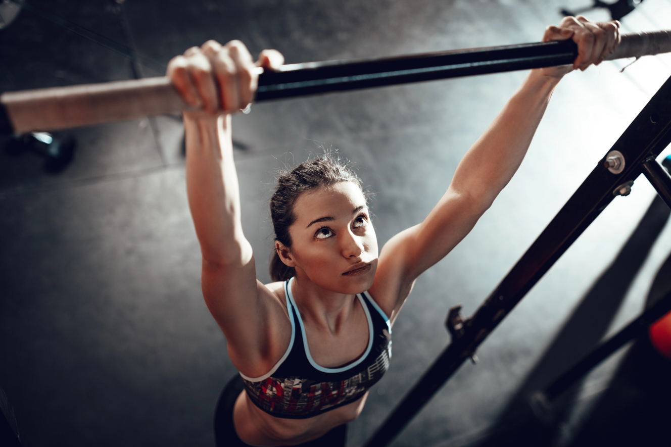 Frau trainiert Klimmzüge an einer Stange im Fitnessstudio und bereitet sich auf ihren ersten Klimmzug vor