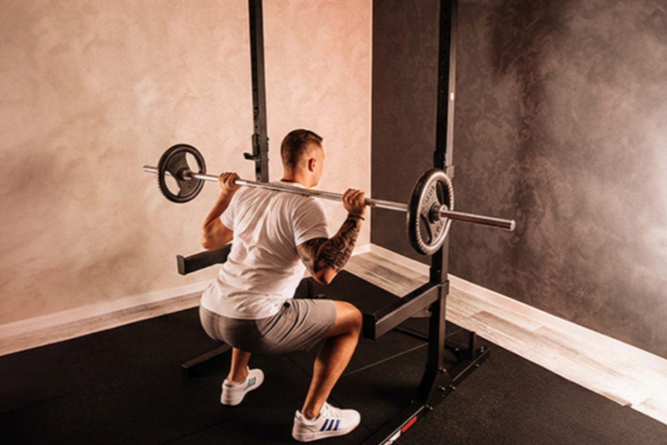 Mann führt Kniebeugen mit einer Langhantel in einem stabilen Squat Rack für effektives Beintraining zuhause aus.