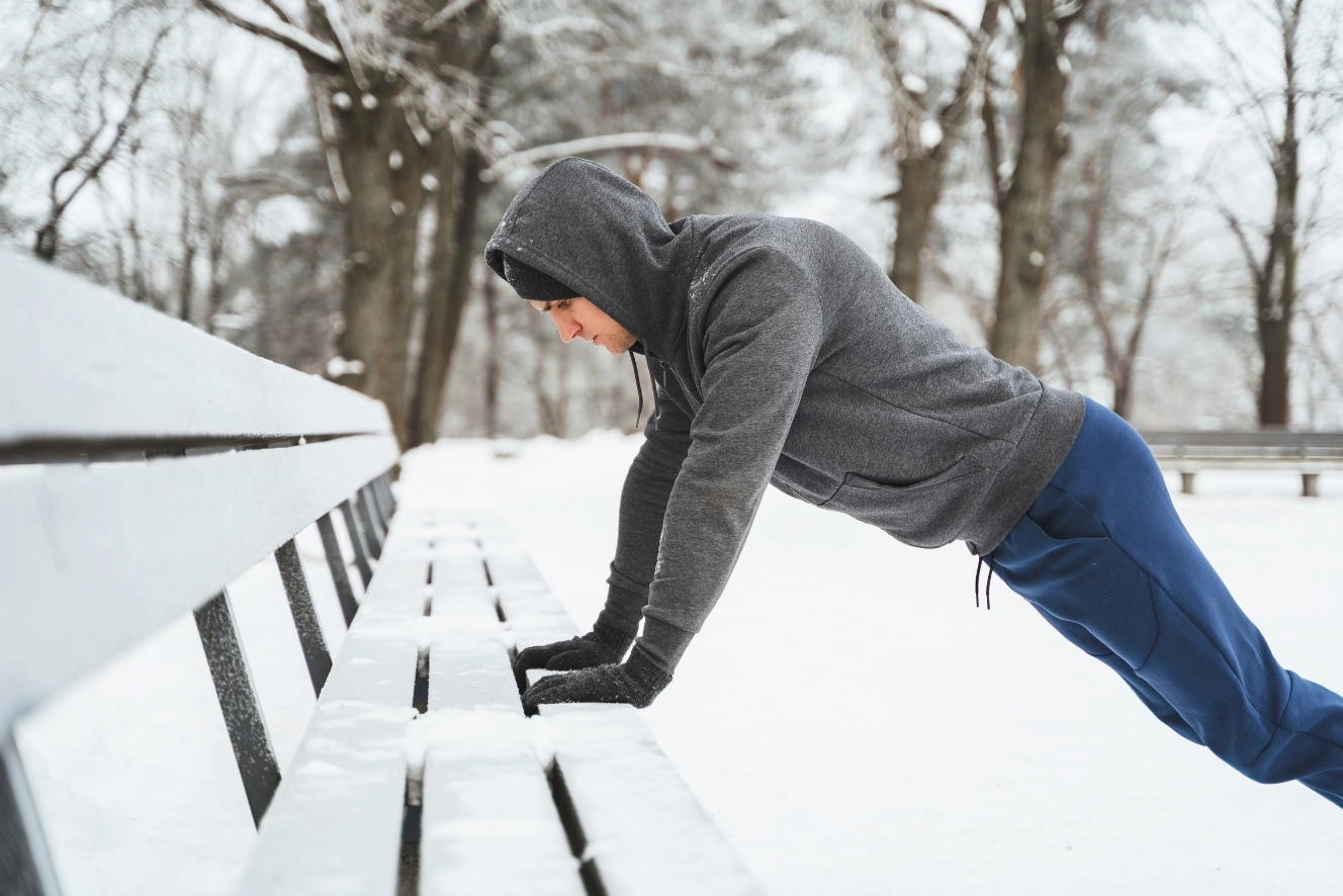 Mann macht Liegestütze an einer Parkbank im Schnee und überwindet das Wintertief beim Training